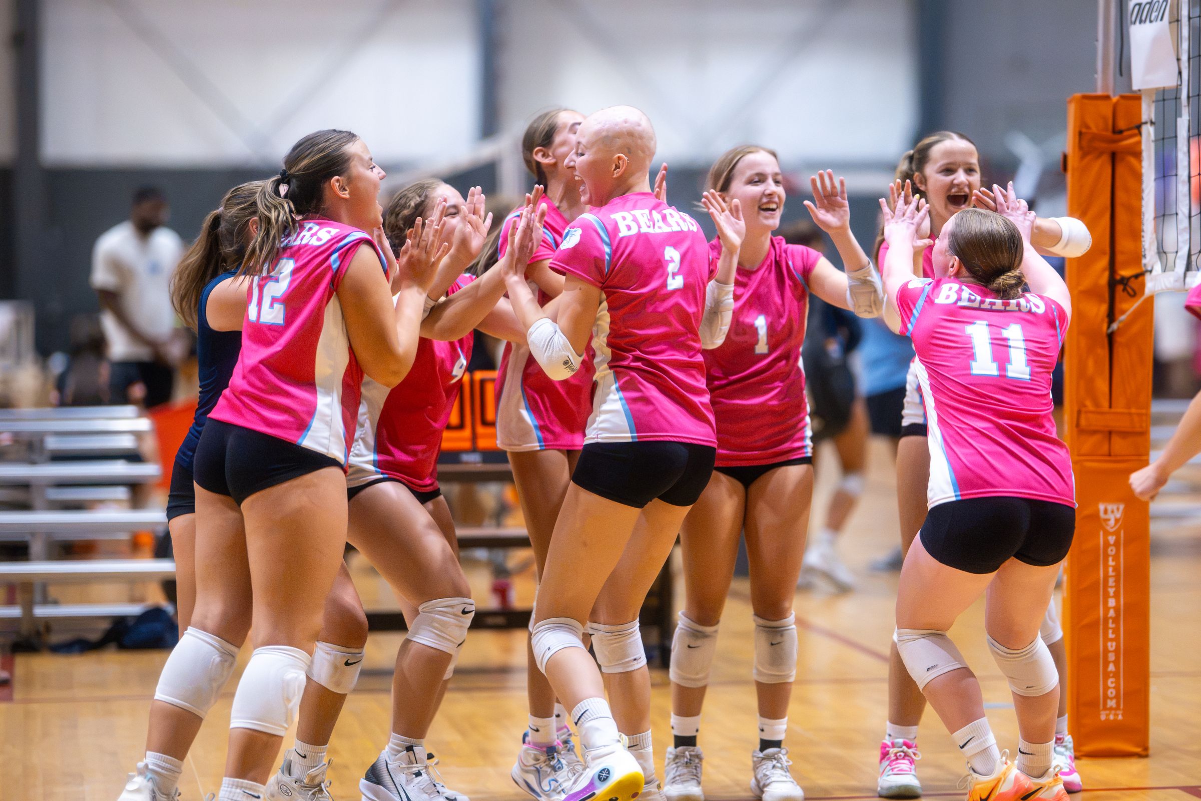 A team in pink jerseys jumps and high-fives after winning a point at the PNW SVC